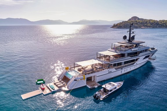 Motor yacht PARA BELLUM at anchor in late-afternoon light with the beach club open and tender alongside