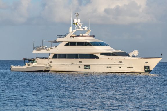Two megayachts lying at anchor in clear water off Mustique in the Grenadines, green hills behind