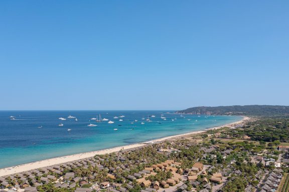 Aerial view along Pampelonne beach at Ramatuelle near Saint-Tropez, a long sweep of pale sand between pine covered dunes and turquoise shallows, with motor yachts and sailing yachts anchored offshore